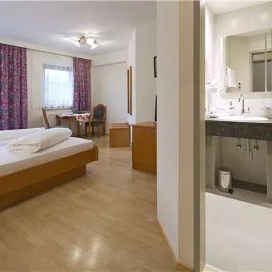 Ein einfaches Zimmer mit einem Bett, einem Tisch und Stühlen. Das Badezimmer ist modern und neben dem Schlafbereich.