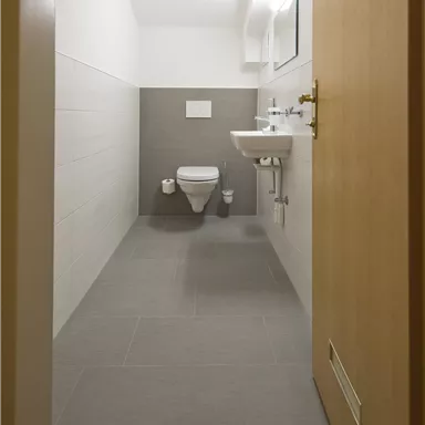 Ein modernes Badezimmer mit einem WC und einem Waschbecken. Der Raum hat helle Fliesen und eine minimalistische Gestaltung.