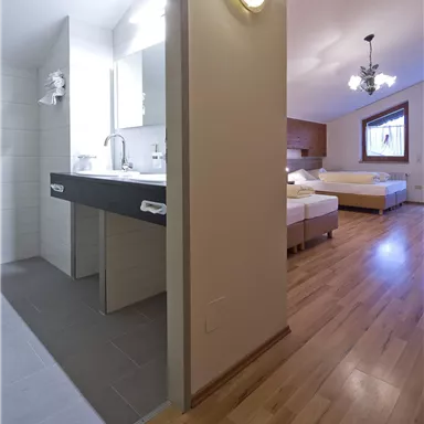 Ein modernes Zimmer mit zwei Betten und einem angrenzenden Badezimmer. Der Boden ist aus hellem Holz und das Licht ist freundlich.