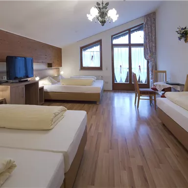 Ein geräumiges Zimmer mit zwei Einzelbetten und einem Doppelbett. Es gibt einen TV, einen Tisch und große Fenster, die viel Licht hereinlassen.