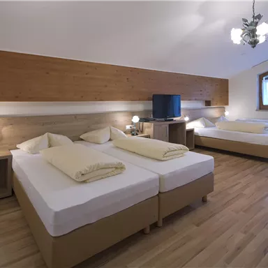Ein gemütliches Hotelzimmer mit zwei Einzelbetten und einem Doppelbett. Die Einrichtung ist modern und hell, mit Holzpanelen und einem großen Fenster.