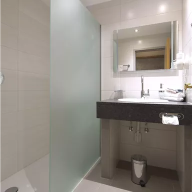 Ein modernes Badezimmer mit einer durchsichtigen Duschabtrennung und einem eleganten Waschbecken. Die Wände sind hell und die Beleuchtung ist freundlich.