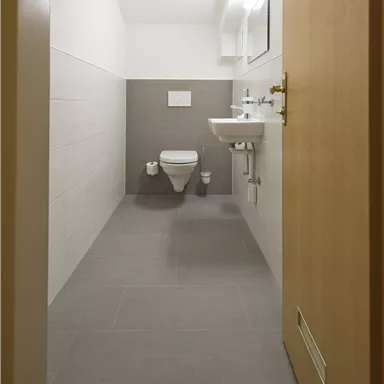 Ein modernes Badezimmer mit einem WC und einem Waschbecken. Die Wände sind hell und die Bodenfliesen sind grau.