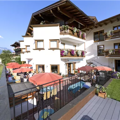 Ein einladendes Hotel mit Terrassen und Sonnenschirmen. Die Umgebung ist grünt und die Berge sind im Hintergrund sichtbar.