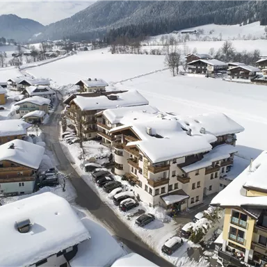 Eine verschneite Landschaft mit charmanten Häusern. Im Hintergrund sind schneebedeckte Berge und ein klarer Himmel zu sehen.