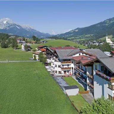Eine malerische Landschaft mit grünen Wiesen und Berge im Hintergrund. Das Bild zeigt ein ruhiges Dorf mit traditionellen Gebäuden.