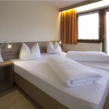 Ein helles und modernes Schlafzimmer mit einem Doppelbett und komfortablen Kissen. Große Fenster sorgen für viel Tageslicht und eine einladende Atmosphäre.