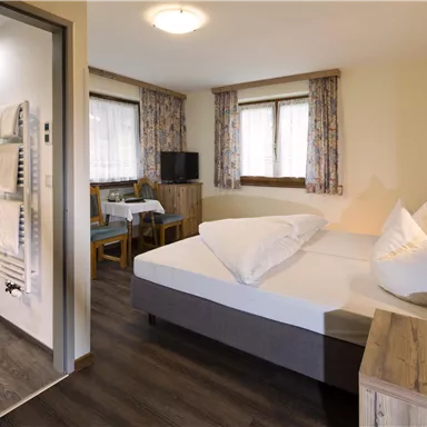 Ein gemütliches Schlafzimmer mit einem Doppelbett und zwei Kissen. Im Hintergrund sind ein Tisch, Stühle und ein Badezimmer sichtbar.