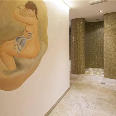 Ein moderner Innenraum mit einer künstlerischen Wandmalerei einer sitzenden Figur. Die Wände sind mit glatten Fliesen und geschwungenen Säulen dekoriert.