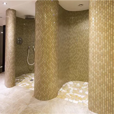 Eine moderne Dusche mit mosaikverkleideten Wänden und eleganten Säulen. Der Boden ist aus hellem Stein und sorgt für ein stilvolles Ambiente.