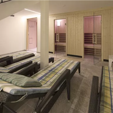 Ein entspannender Raum mit Liegen und Holzsaunen. Die Wände sind hell und die Atmosphäre wirkt beruhigend.