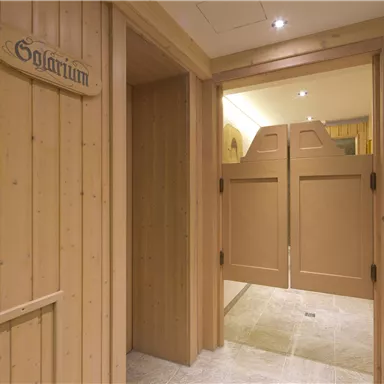 Ein gemütlicher Raum mit holzverkleideten Wänden und einem Schild mit der Aufschrift "Solarium". Der Eingang ist hell beleuchtet und führt zu einem weiteren Bereich.