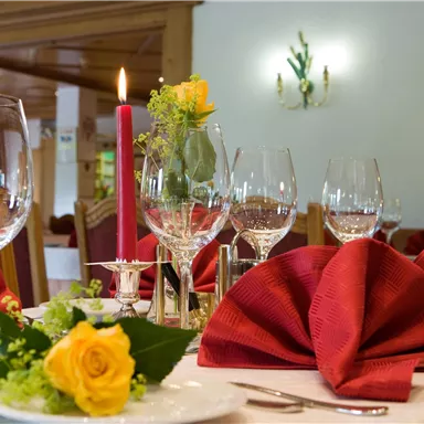 Ein elegant gedeckter Tisch mit roten Servietten und Weingläsern. Eine Rose und eine Kerze sorgen für eine romantische Atmosphäre.