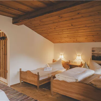 Ein gemütliches Zimmer mit Holzdecke und zwei Betten. Es gibt einen Tisch mit Stühlen und warmes Licht von den Wandleuchten.