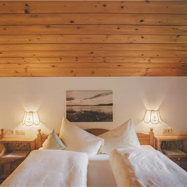 Ein gemütliches Schlafzimmer mit Holzwänden und einem Holzdecke. Die Betten sind mit weißen Bettwäsche und Kissen dekoriert, und sanftes Licht kommt von den Nachttischlampen.