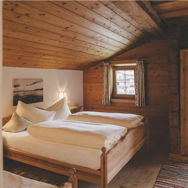 Ein gemütliches Zimmer mit Holzverkleidung und zwei Betten. Es gibt ein Fenster mit Blick nach außen und warmes Licht von einer Tischlampe.