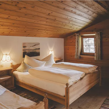 Ein gemütliches Schlafzimmer mit Holzvertäfelungen und zwei Betten. Sanfte Beleuchtung und ein Fenster sorgen für eine einladende Atmosphäre.