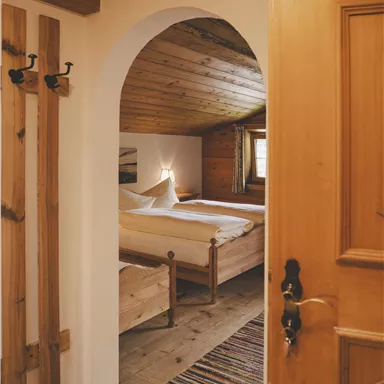 Ein gemütliches Schlafzimmer mit Holzverkleidung und einem großen Bett. Die Atmosphäre ist warm und einladend, mit einem bunten Teppich im Eingangsbereich.