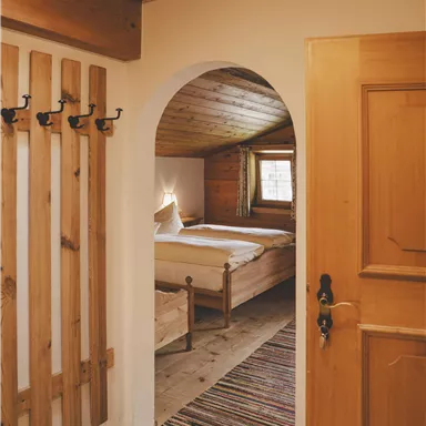 Ein gemütlicher Flur mit Holzdetails und einem bunten Teppich. Im Hintergrund ist ein einladendes Schlafzimmer sichtbar.