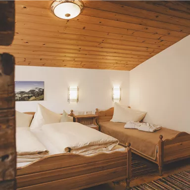 Ein gemütliches Zimmer mit Holzbetten und einem warmen, einladenden Ambiente. Die Wände sind hell, und die Decke ist aus Holz, was eine gemütliche Atmosphäre schafft.