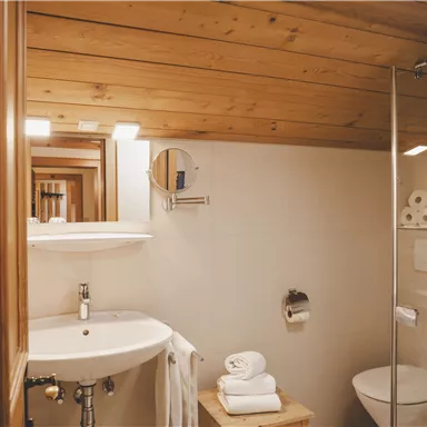 Ein modernes Badezimmer mit Holzdecke, einem Waschbecken und einer gläsernen Dusche. Saubere Handtücher und Toilettenpapier sind gut sichtbar.