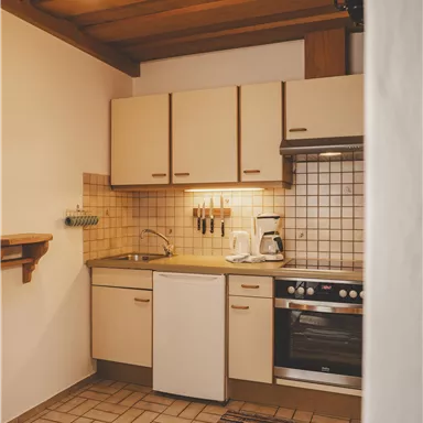 Eine moderne Küche mit Holzdecken und hellen Möbeln. Die Küche ist gut ausgestattet mit Herd, Kühlschrank und elektrischen Geräten.