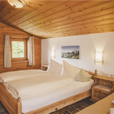 Ein gemütliches Schlafzimmer mit Holzvertäfelung und einem großen Doppelbett. Es gibt ein Fenster, das viel Licht hereinlässt, sowie moderne Lampen an den Wänden.