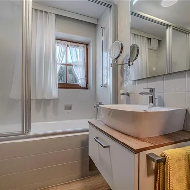 Ein modernes Badezimmer mit einer Badewanne und einem Waschbecken. Helle Farben und natürliche Lichtquellen sorgen für eine angenehme Atmosphäre.