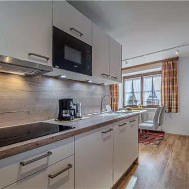 Eine moderne Küche mit hellen, minimalistischen Möbeln und Holzoberflächen. Das Fenster lässt viel Tageslicht herein und bietet einen Ausblick auf die Umgebung.