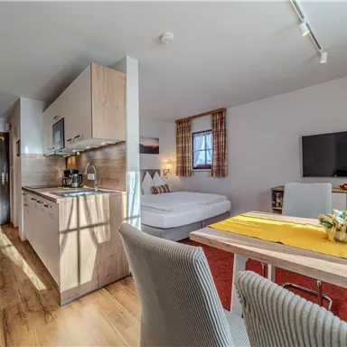 Eine moderne Wohnung mit offener Küche, Essbereich und Schlafbereich. Der Raum ist hell und freundlich mit Holzfußboden und großen Fenstern.