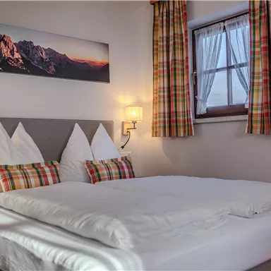 Ein gemütliches Schlafzimmer mit einem großen Bett und karierten Vorhängen. An der Wand hängt ein Bild von Bergen.