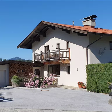 Ein charmantes Haus mit einem roten Satteldach und einem schön gestalteten Außenbereich. Umgeben von grünen Bäumen und Blumen bietet es eine einladende Atmosphäre.