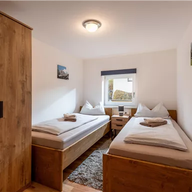 A cozy room with two single beds and wooden interior. The window offers a view outside and the room is brightly lit.