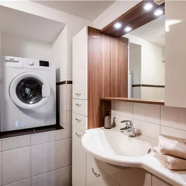 A modern bathroom with a washing machine and a sink. There are bright tiles and wooden details.