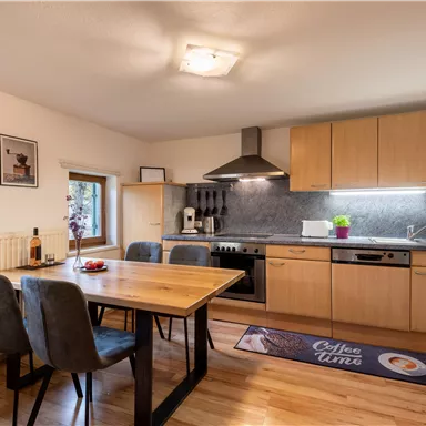 A modern kitchen with a dining table and chairs. The wooden surfaces and gray accents give it a cozy look.