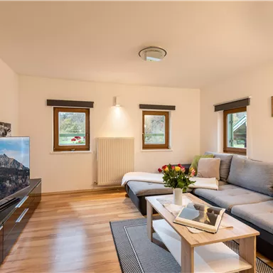 A cozy living room with bright walls and a wooden floor. There is a large sofa, a television, and decorative elements.