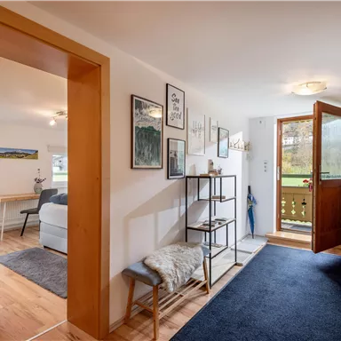 An inviting entrance area with wooden doors and modern decor. The room has a carpet and offers a view of a seating area.
