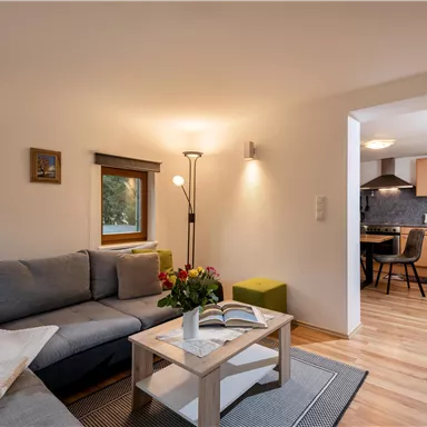 A modern living room with a gray sofa and a table. Through an open space, the kitchen is visible, which is well equipped.