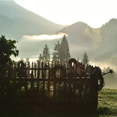 A picturesque landscape with a wooden picket fence and mountains in the background. The fog adds a mystical atmosphere to the scene.