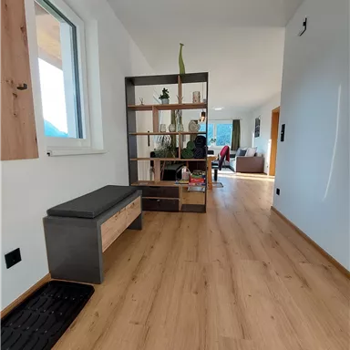 Ein heller Flur mit Holzfußboden und einer modernen Regalwand. Im Hintergrund ist ein gemütlicher Wohnbereich sichtbar.