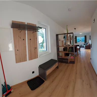 Ein heller Flur mit Holzfußboden und modernen Möbeln. An der Wand befinden sich ein Garderobenständer und ein Regal.