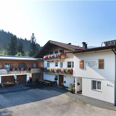 Ein gemütliches Gästehaus in einer bergigen Umgebung. Das Gebäude hat Balkone mit Blumen und eine helle Fassade.