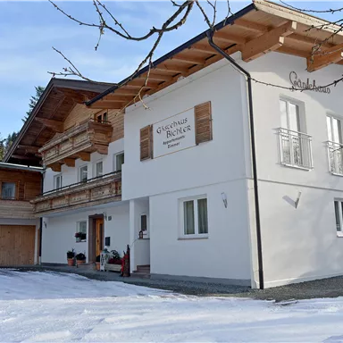 Ein modernes Haus im alpinen Stil, umgeben von Schnee und Bäumen. Die Fassade ist hell und einladend, mit Holzdetails.