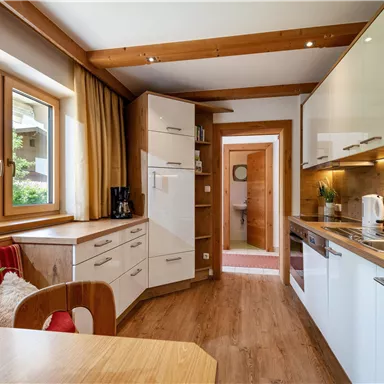 Eine moderne Küche mit Holz- und weißen Möbeln. Große Fenster sorgen für viel Tageslicht und eine freundliche Atmosphäre.