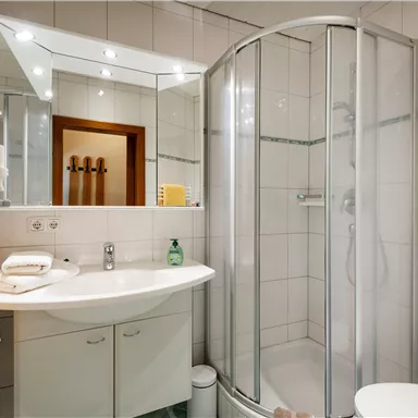 Ein modernes Badezimmer mit einer Duschkabine und einem Waschbecken. Die Wände sind gefliest, und es gibt weiche Handtücher in Gelb.