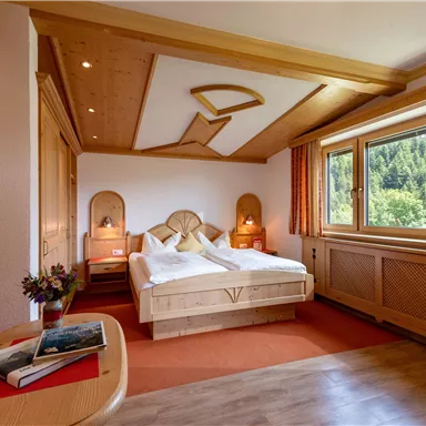 Ein gemütliches Schlafzimmer mit einem Doppelbett und Holzverkleidung. Große Fenster bieten einen schönen Blick ins Grüne.