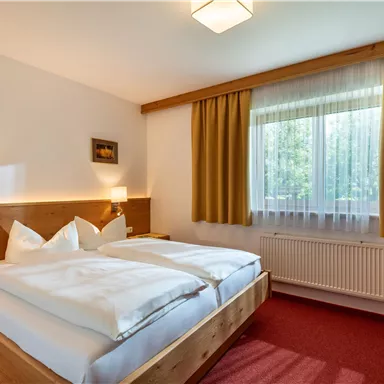 Ein gemütliches Hotelzimmer mit zwei Betten und warmen Holzdetails. Große Fenster lassen viel Tageslicht herein und sorgen für eine einladende Atmosphäre.