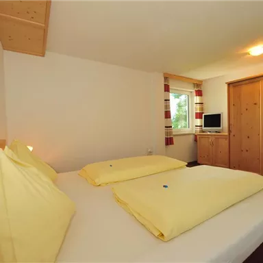 A cozy bedroom with two beds and yellow pillows. The room has wooden details and a television on a desk.