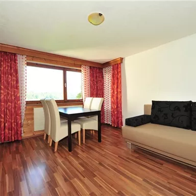 A bright living room with wooden flooring and modern furniture. There is a table with chairs and a sofa corner that creates a pleasant atmosphere.