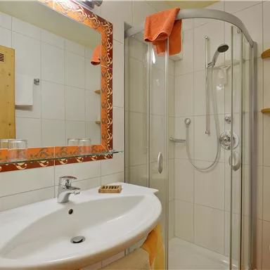 Ein modernes Badezimmer mit einer Dusche und einem Waschbecken. An der Wand hängt ein dekorativer Spiegel und es gibt Holzregale.